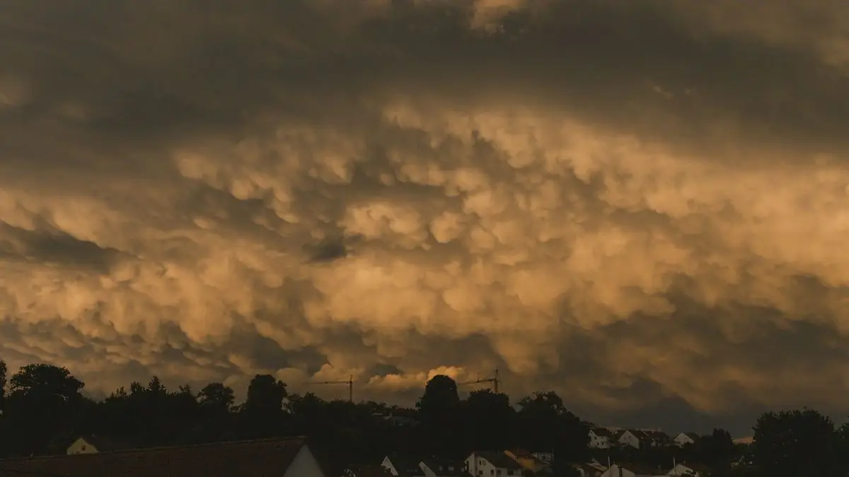 Heavy storm clouds lit orange above rooftops