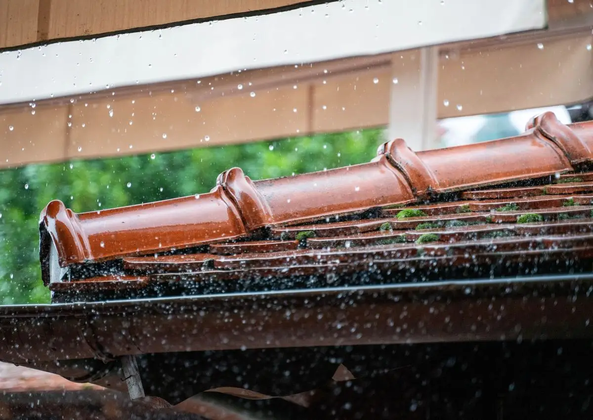 Rain falling on a tiled roof edge and gutter